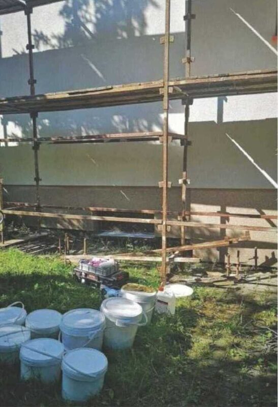 Gerüst mit Arbeitsmaterial und Farbeimern auf dem Rasen vor der Fassade